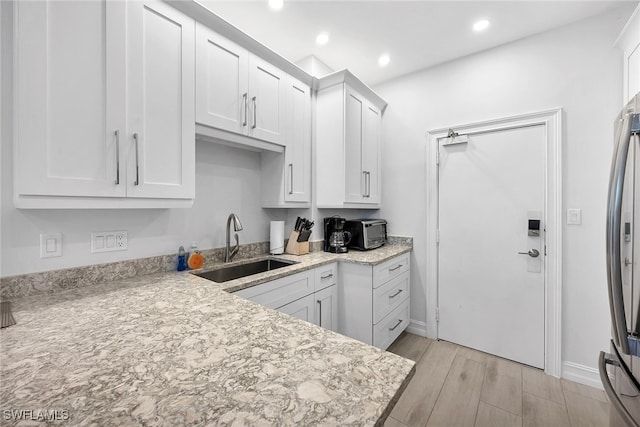 kitchen with light stone counters, white cabinets, sink, light hardwood / wood-style flooring, and stainless steel fridge