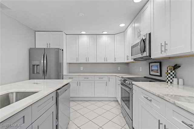 kitchen with white cabinetry, stainless steel appliances, light tile patterned flooring, and light stone countertops