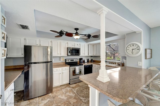 kitchen featuring ornate columns, white cabinets, kitchen peninsula, a kitchen breakfast bar, and appliances with stainless steel finishes