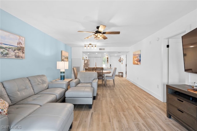 living room featuring light wood finished floors, baseboards, visible vents, and a ceiling fan