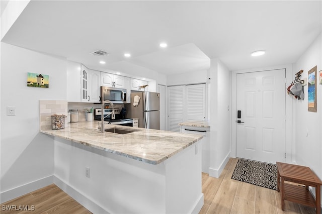 kitchen with stainless steel appliances, a peninsula, visible vents, light wood-type flooring, and light stone countertops