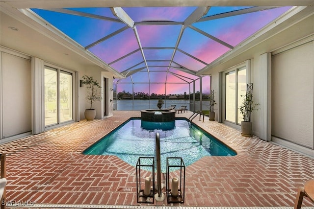 pool at dusk featuring a patio, glass enclosure, and an in ground hot tub