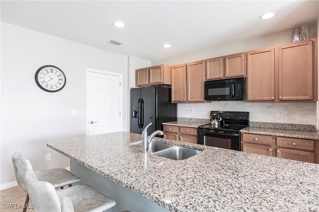 kitchen with tasteful backsplash, sink, a kitchen bar, black appliances, and light stone countertops