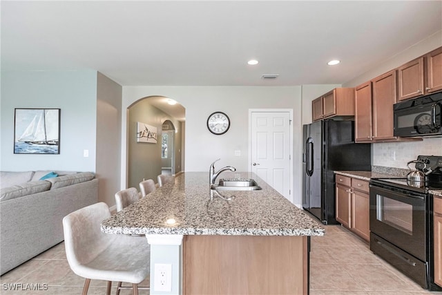 kitchen with sink, light tile patterned floors, a kitchen island with sink, black appliances, and a kitchen bar