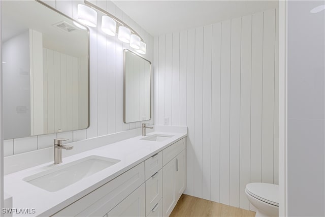 bathroom with hardwood / wood-style floors, vanity, wood walls, and toilet