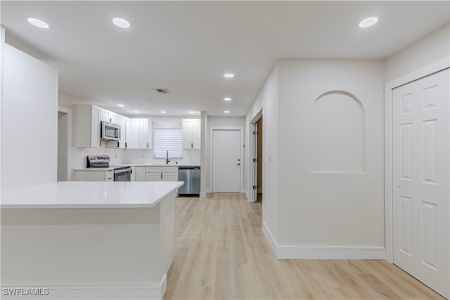 kitchen featuring stainless steel appliances, kitchen peninsula, light hardwood / wood-style floors, decorative backsplash, and white cabinets