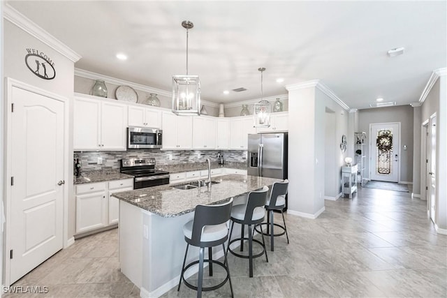 kitchen featuring stainless steel appliances, a sink, white cabinets, a center island with sink, and decorative light fixtures