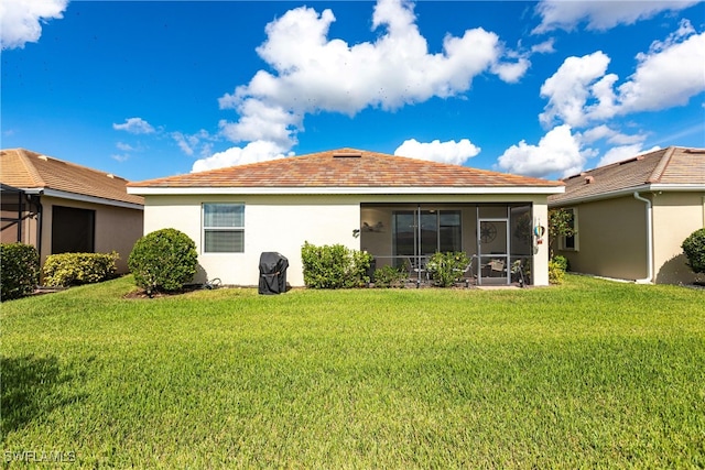 back of house featuring a sunroom, a yard, and stucco siding