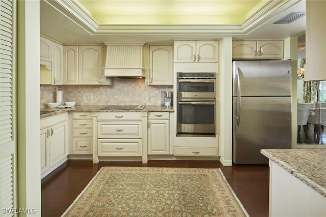 kitchen with a tray ceiling, appliances with stainless steel finishes, custom range hood, and light stone counters