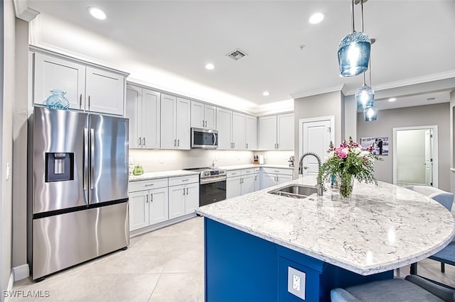 kitchen with stainless steel appliances, a center island with sink, light stone counters, sink, and decorative light fixtures