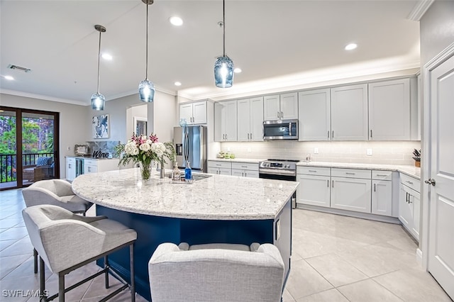 kitchen featuring pendant lighting, appliances with stainless steel finishes, an island with sink, and light stone countertops