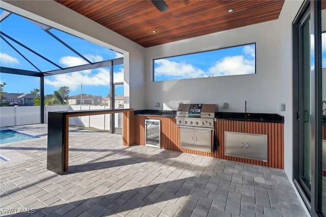 view of patio / terrace featuring sink, glass enclosure, grilling area, beverage cooler, and exterior kitchen