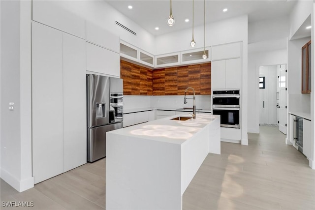 kitchen featuring a kitchen island with sink, white cabinetry, stainless steel appliances, and decorative light fixtures