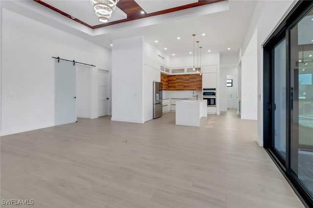 unfurnished living room featuring sink, crown molding, a barn door, and a high ceiling