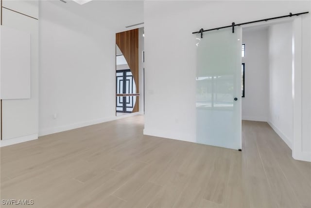 unfurnished room with a barn door and light hardwood / wood-style floors