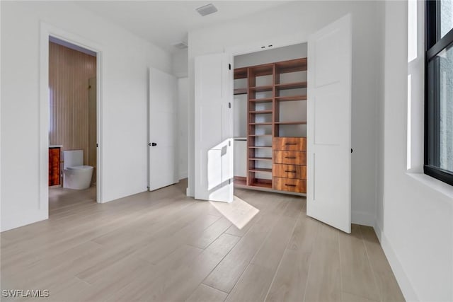 unfurnished bedroom featuring ensuite bath, light hardwood / wood-style floors, and a closet