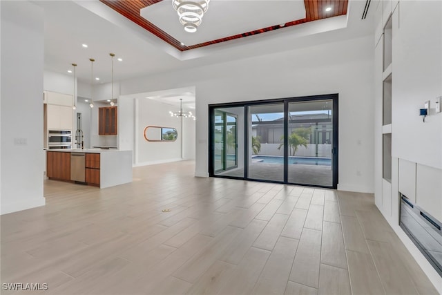 unfurnished living room featuring a raised ceiling and an inviting chandelier