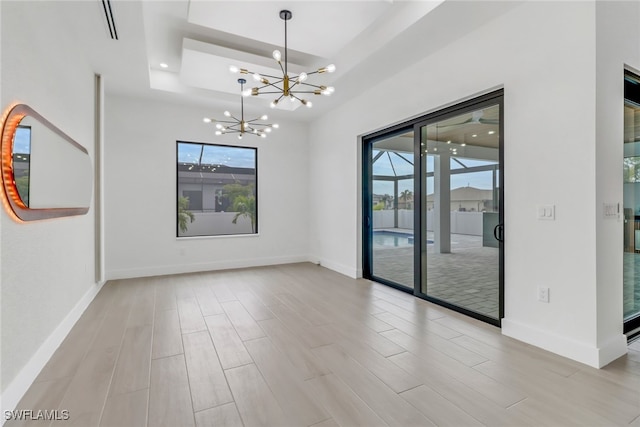 spare room featuring a tray ceiling and a chandelier