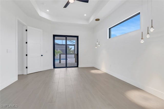 empty room with a raised ceiling, ceiling fan, and light hardwood / wood-style flooring