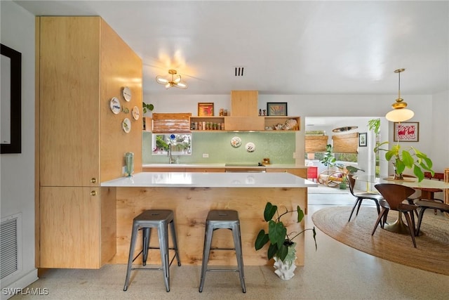 kitchen featuring visible vents, a breakfast bar area, light countertops, a peninsula, and a sink