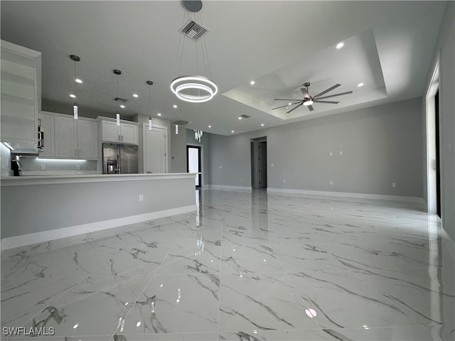 unfurnished living room featuring ceiling fan and a tray ceiling