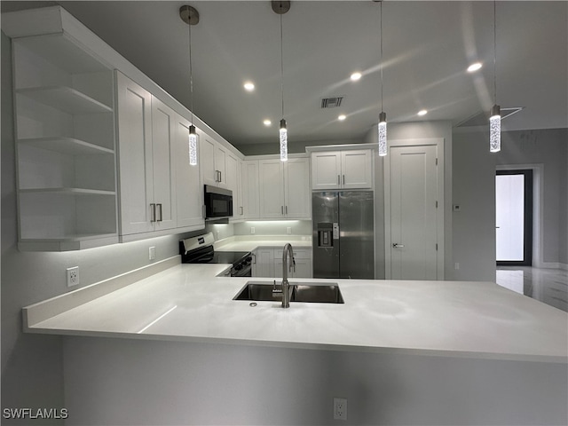 kitchen with white cabinetry, sink, kitchen peninsula, appliances with stainless steel finishes, and decorative light fixtures