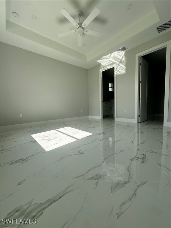 empty room featuring ceiling fan and a raised ceiling