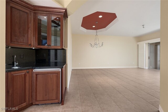 bar featuring decorative backsplash, a tray ceiling, sink, light tile patterned floors, and a chandelier