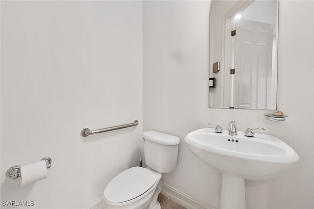 half bathroom featuring tile patterned floors, a sink, toilet, and baseboards