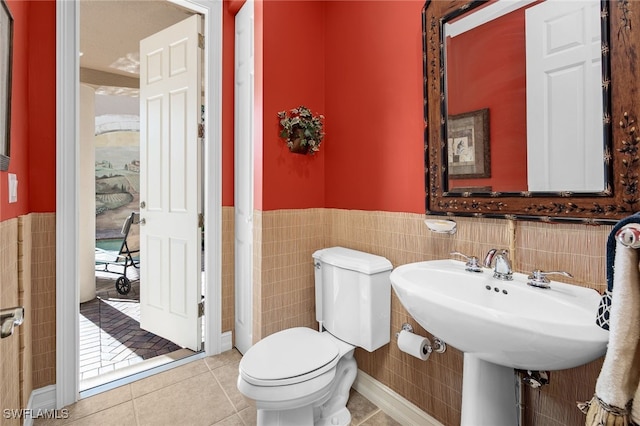 half bath featuring toilet, wainscoting, tile walls, and tile patterned floors