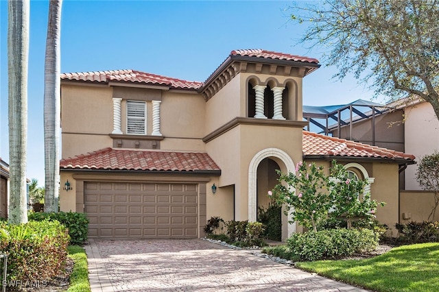 mediterranean / spanish-style house with decorative driveway, a tile roof, a lanai, and stucco siding