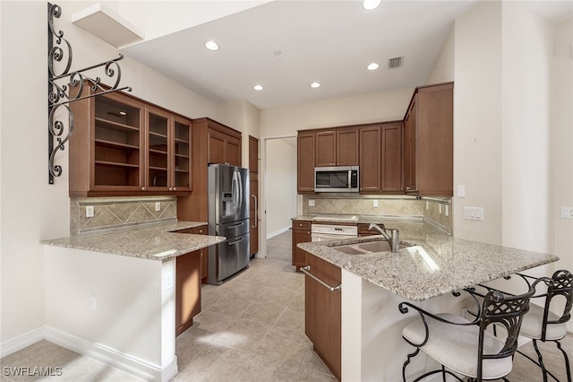 kitchen with a kitchen bar, light stone countertops, kitchen peninsula, and stainless steel appliances