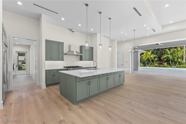 kitchen with hanging light fixtures, wall chimney exhaust hood, light hardwood / wood-style floors, and plenty of natural light