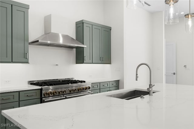 kitchen featuring light stone countertops, wall chimney exhaust hood, decorative light fixtures, green cabinetry, and high end stove