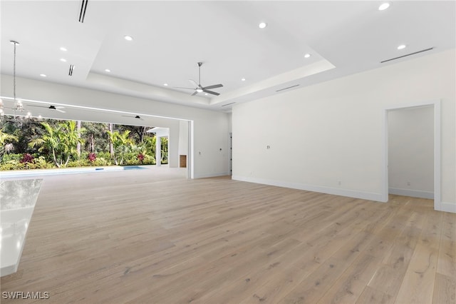 unfurnished living room featuring light wood-type flooring, a tray ceiling, and ceiling fan with notable chandelier