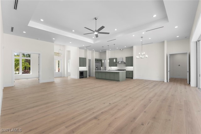 unfurnished living room featuring ceiling fan with notable chandelier, a raised ceiling, light wood-type flooring, and sink