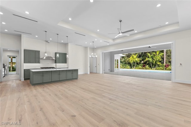 living room with ceiling fan with notable chandelier, light hardwood / wood-style flooring, and a tray ceiling