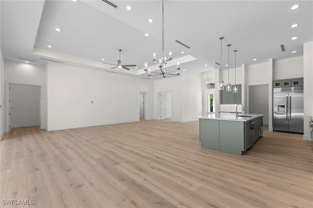 kitchen featuring sink, an island with sink, a raised ceiling, light hardwood / wood-style flooring, and built in fridge