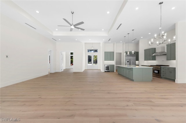 kitchen featuring decorative light fixtures, an island with sink, light hardwood / wood-style floors, high quality appliances, and wall chimney exhaust hood