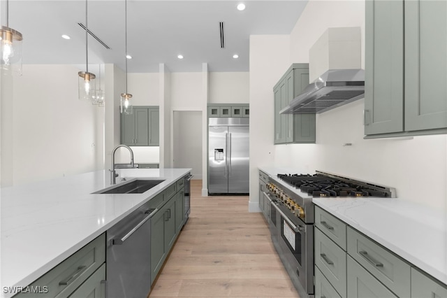 kitchen featuring premium appliances, decorative light fixtures, sink, and wall chimney exhaust hood