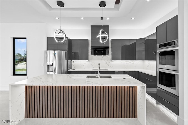 kitchen featuring decorative light fixtures, sink, stainless steel appliances, and an island with sink