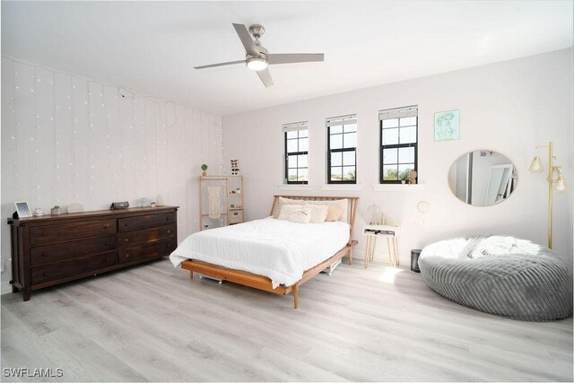 bedroom with ceiling fan, wood walls, and light hardwood / wood-style flooring