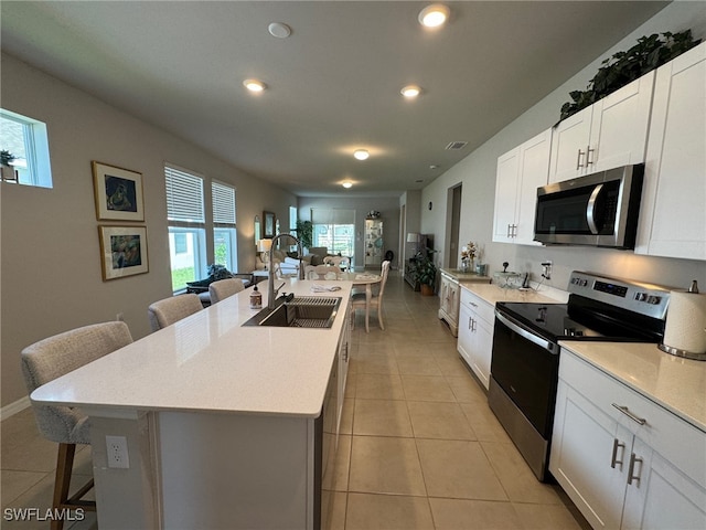 kitchen featuring appliances with stainless steel finishes, a center island with sink, a breakfast bar, and plenty of natural light