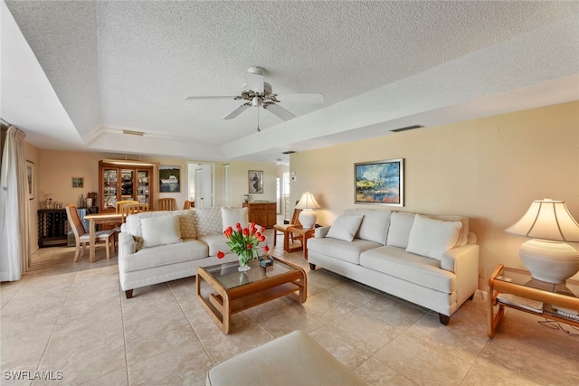 living room with light tile patterned flooring, a textured ceiling, ceiling fan, and a raised ceiling