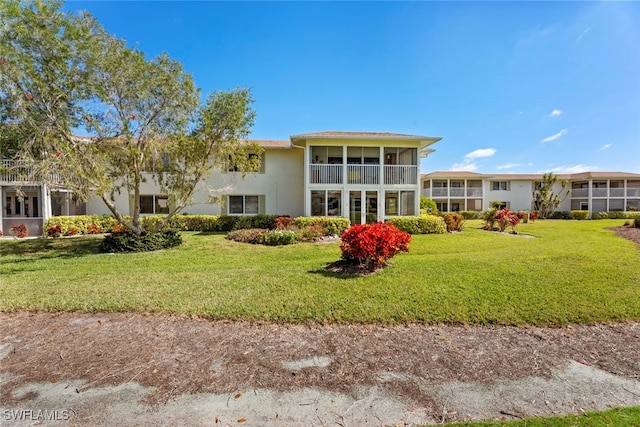 back of property featuring a balcony, a sunroom, and a yard