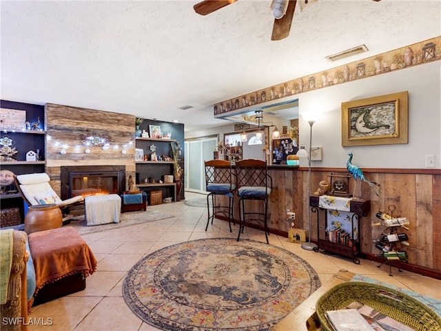 living room featuring built in features, a large fireplace, wood walls, and a textured ceiling