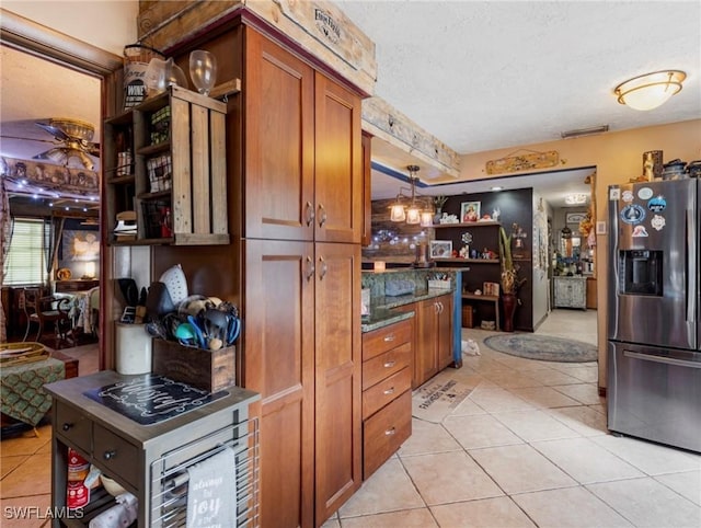 kitchen featuring dark stone countertops, stainless steel refrigerator with ice dispenser, light tile patterned flooring, hanging light fixtures, and a textured ceiling