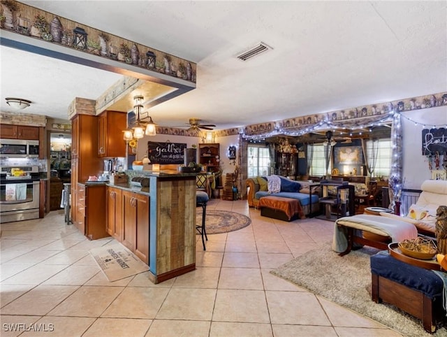 kitchen with decorative light fixtures, ceiling fan, a kitchen bar, light tile patterned flooring, and stainless steel appliances