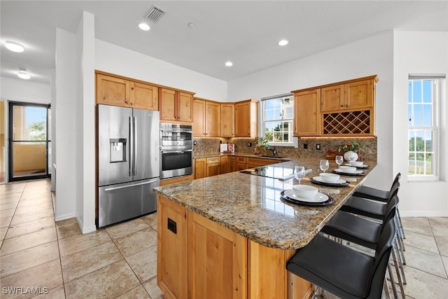 kitchen with kitchen peninsula, tasteful backsplash, stone counters, a breakfast bar area, and stainless steel appliances