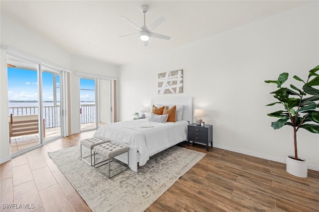 bedroom featuring wood-type flooring, a water view, ceiling fan, and access to outside